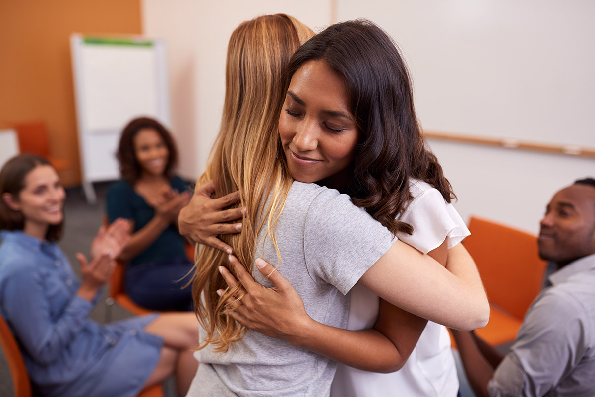 Close up of two women hugging during a 12 Step Program meeting.