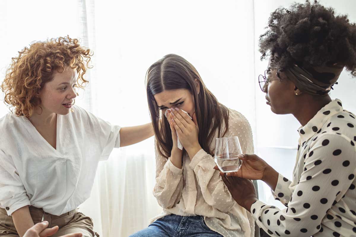 Supportive women comforting a friend during addiction therapy session.