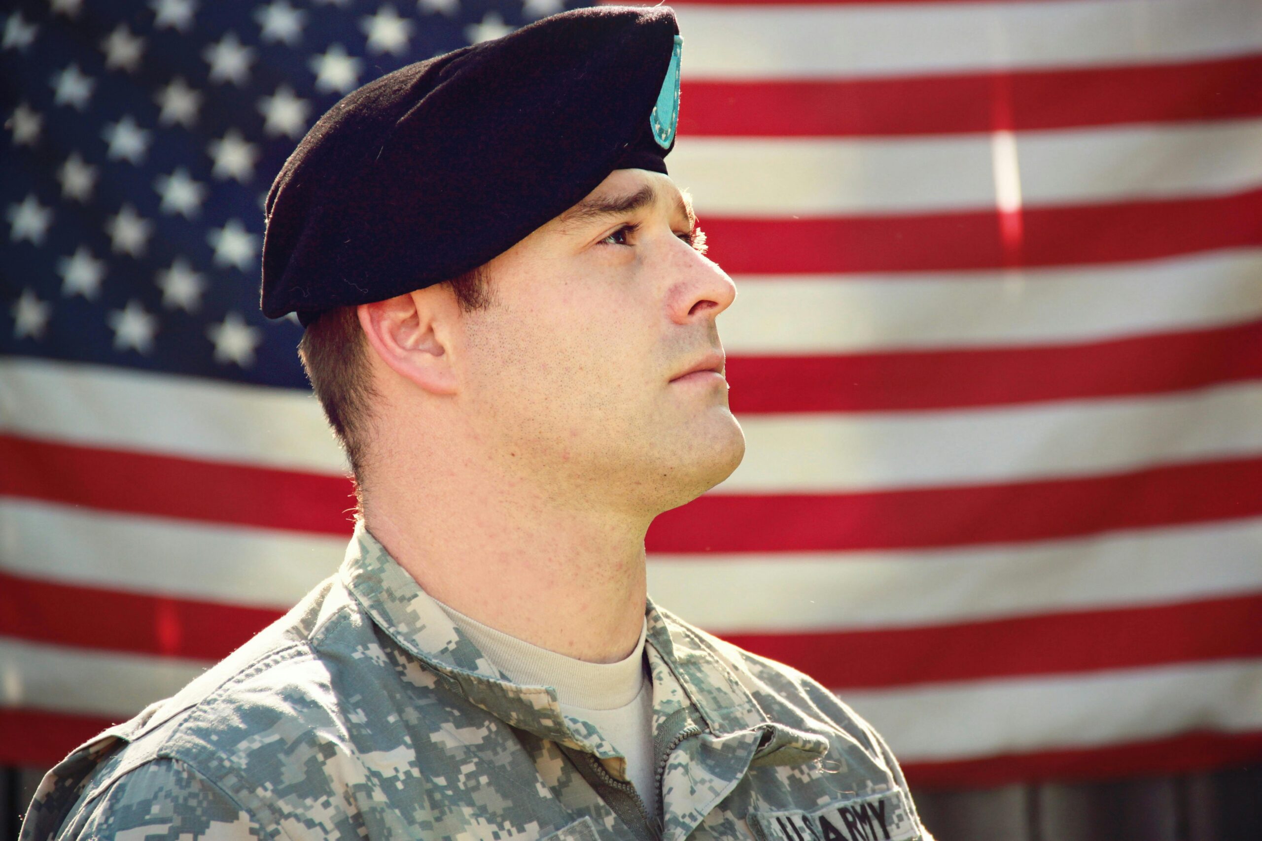 Close up of a veteran looking off into the distance with an American flag in the background symbolizing the need for veteran addiction treatment in Fresno.